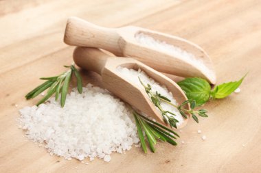 Salt in shovels with fresh basil, rosemary and thyme on wooden background clipart