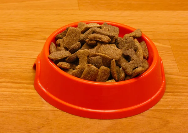 Cibo secco per cani in una ciotola arancione sul pavimento — Foto Stock