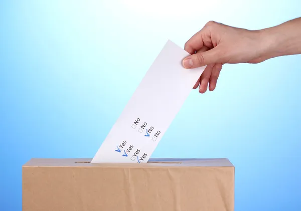 Mano con scheda elettorale e scatola su sfondo blu — Foto Stock