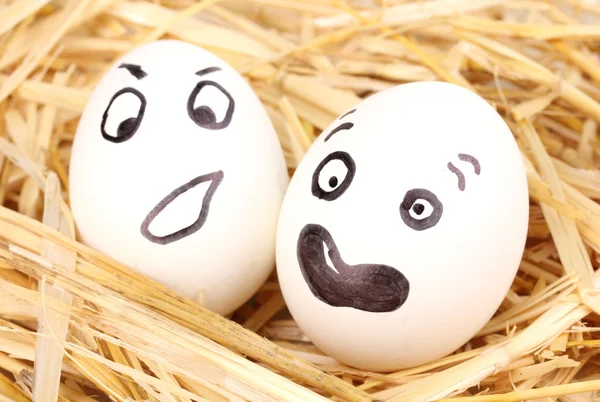 White eggs with funny faces in straw — Stock Photo, Image