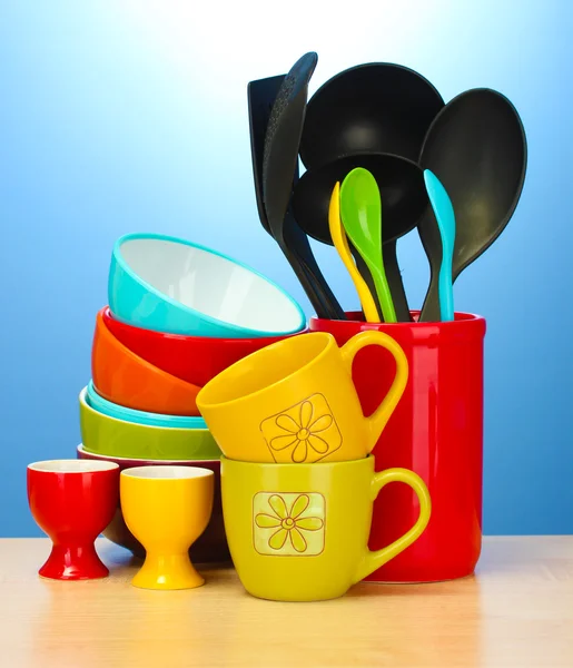 Cuencos vacíos brillantes, tazas y utensilios de cocina sobre mesa de madera sobre fondo azul —  Fotos de Stock