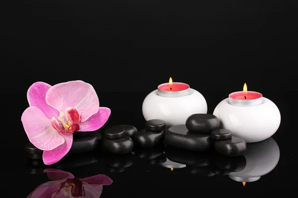 Pietre termali con fiore di orchidea e candele isolate su nero — Foto Stock