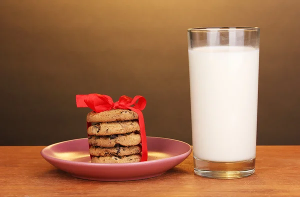 Szklankę mleka i ciasteczka na drewnianym stole na brązowym tle — Zdjęcie stockowe