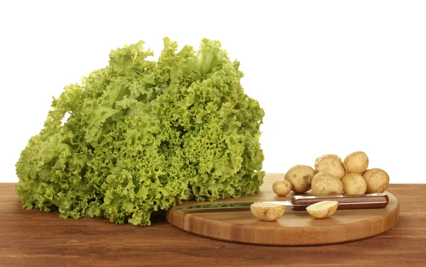 Stock image Young potatoes and lettuce on a cutting board with knife on a table on white background close-up