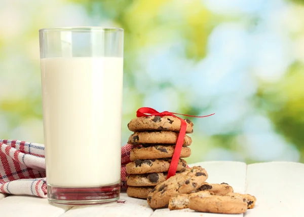 Vaso de leche, galletas de chocolate con cinta roja y flores silvestres sobre mesa de madera sobre fondo verde —  Fotos de Stock