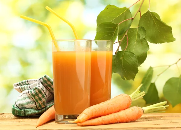 Glasses of carrot juice and fresh carrots on wooden table on green background — Stock Photo, Image