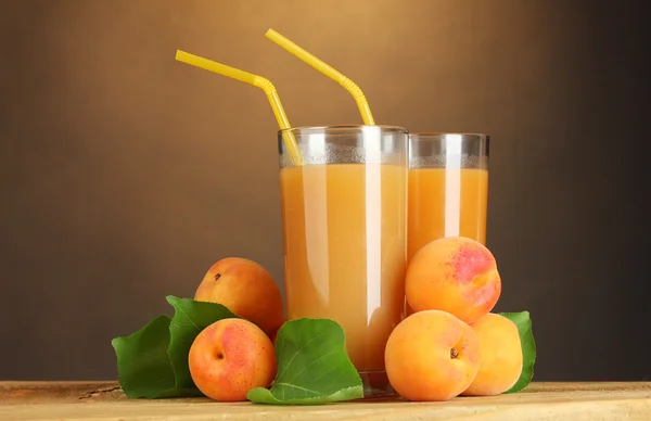 Glasögon av aprikos juice på träbord på brun bakgrund — Stockfoto