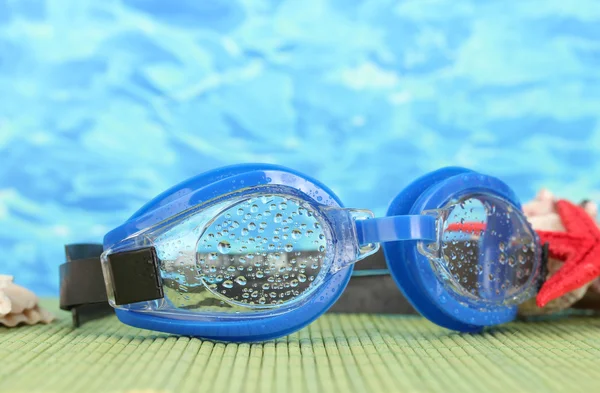 Lunettes de bain bleues avec des gouttes sur un tampon de bambou, sur fond de mer bleue — Photo