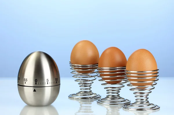 Яйцо таймер и яйцо в металлический стенд на голубом фоне — стоковое фото