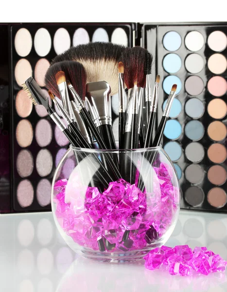 Make-up borstels in een kom met stenen op palet van schaduwen achtergrond — Stockfoto