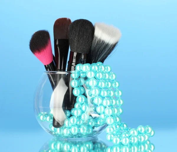 Make-up-Pinsel in einer Schüssel mit Perlenkette auf blauem Hintergrund — Stockfoto