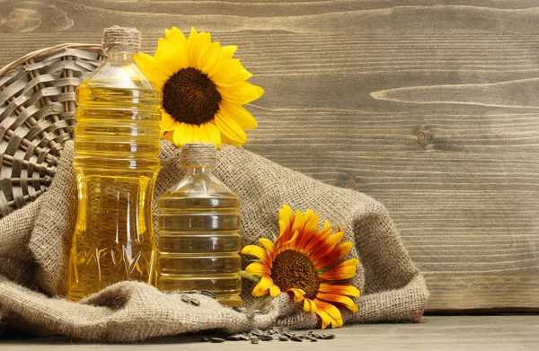 Олія в пляшках, соняшниках і насіннях, на дерев'яному фоні — стокове фото