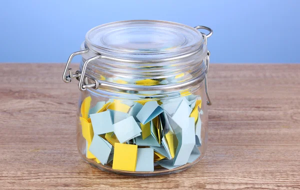 Pieces of paper for lottery in jar on wooden table on blue background — Stock Photo, Image