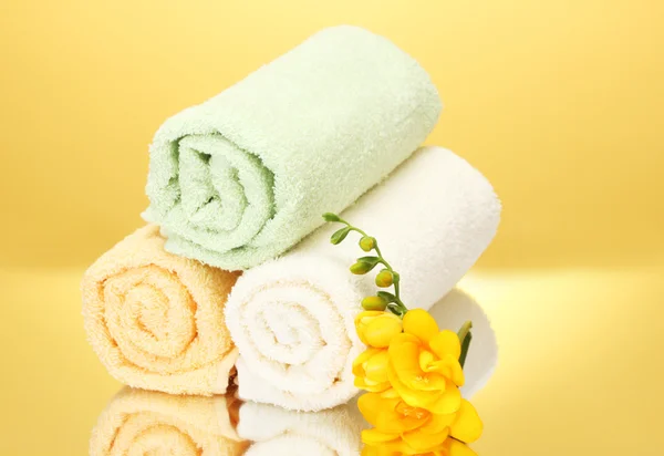 Kolorowe ręczniki i kwiaty na żółtym tle — Zdjęcie stockowe