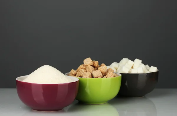 Ciotole con diversi tipi di zucchero su sfondo grigio — Foto Stock