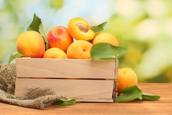 Rijpe abrikozen met bladeren in houten doos op houten tafel op groene achtergrond — Stockfoto