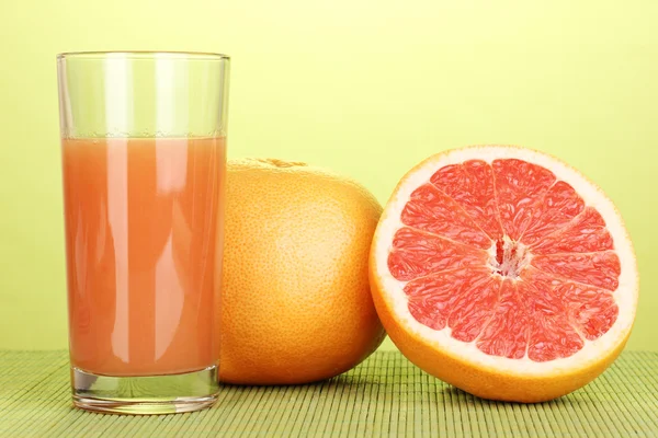 Grapefruit juice and grapefruit on bamboo mat on green background — Stock Photo, Image