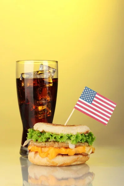 Sanduíche saboroso com bandeira americana e cola, sobre fundo amarelo — Fotografia de Stock