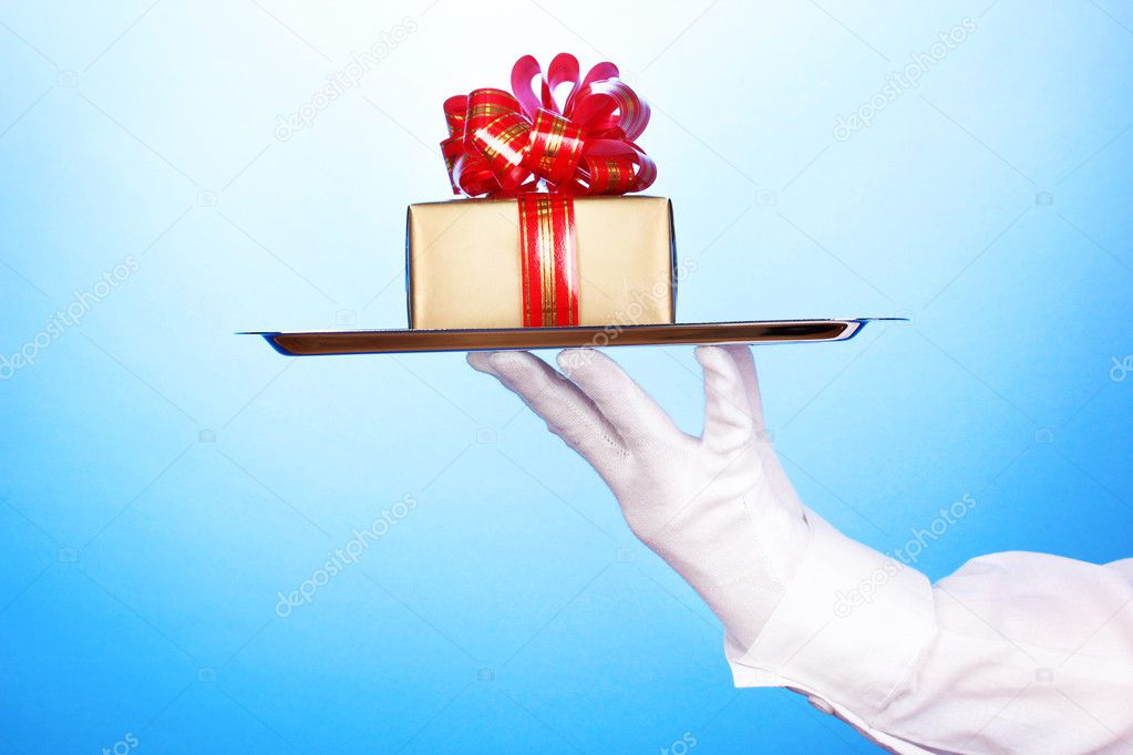 Hand in glove holding silver tray with giftbox on blue background