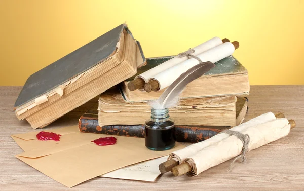 Old books, scrolls, feather pen and inkwell on wooden table on yellow background — Stockfoto