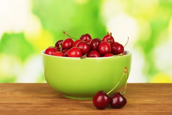 Cherry in green bowl on wooden table on green background — Stock Photo, Image