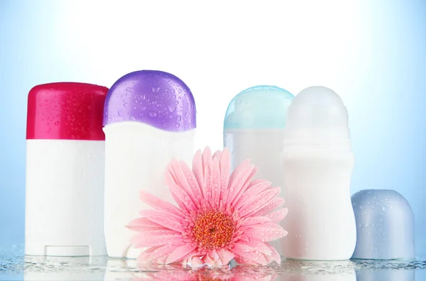 Garrafas desodorantes com flor no fundo azul — Fotografia de Stock