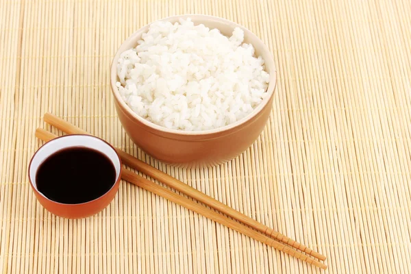 Чаша риса и палочки для еды на бамбуковом коврике — стоковое фото