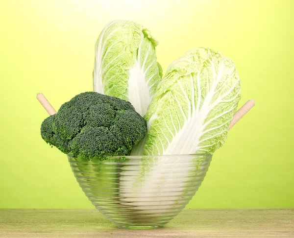 Mangkuk kaca dengan kubis dan brokoli di atas meja kayu dengan latar belakang hijau — Stok Foto