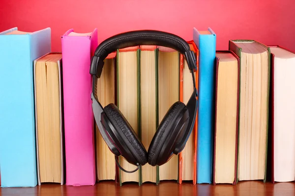 Sluchátka na knihy o dřevěný stůl na růžovém pozadí — Stock fotografie