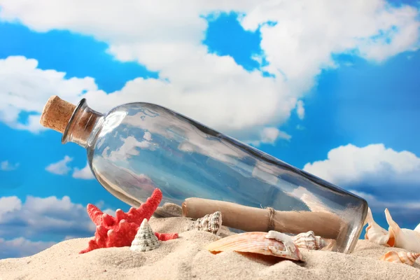 Botella de vidrio con nota en el interior sobre arena, sobre fondo azul cielo — Foto de Stock