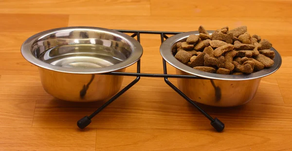 Cibo secco per cani e acqua in ciotole di metallo sul pavimento — Foto Stock