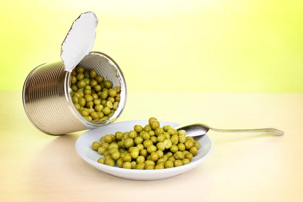 Open tin can and plate with peas and spoon on wooden table on green background — Stock Photo, Image