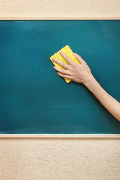Hand with a yellow sponge cleaning the chalkboard — Stock Photo, Image