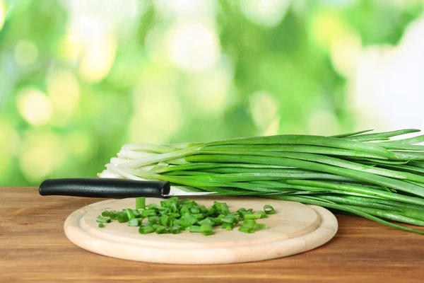 Cipolla verde su un tagliere con coltello su sfondo verde — Foto Stock