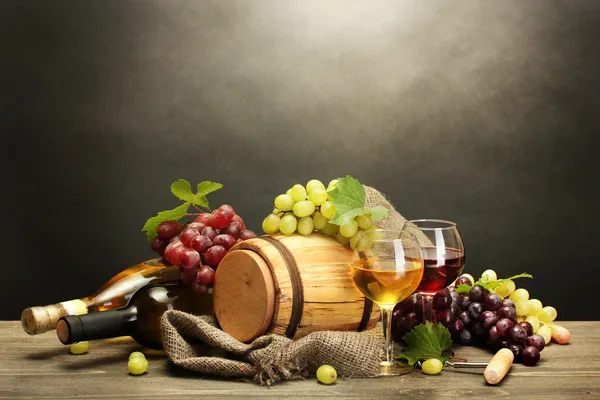 Barril, garrafas e copos de vinho e uvas maduras sobre mesa de madeira sobre fundo cinzento — Fotografia de Stock