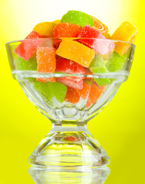 Colorful jelly candies in in glass bowl on green background