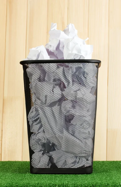 Metal trash bin from paper on grass on wooden background — Stock Photo, Image
