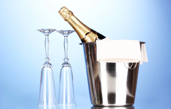 Sektflasche im Eimer mit Eis und Gläsern auf blauem Hintergrund — Stockfoto