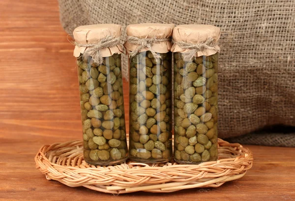 Glass jar with tinned capers on wooden background close-up — Stock Photo, Image