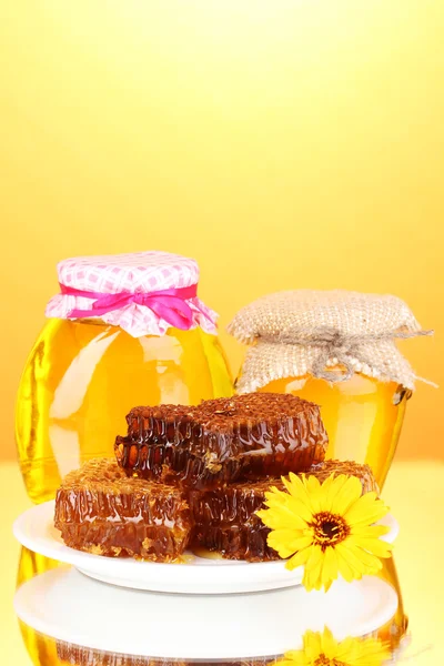 Frascos de mel e favo de mel sobre fundo laranja — Fotografia de Stock