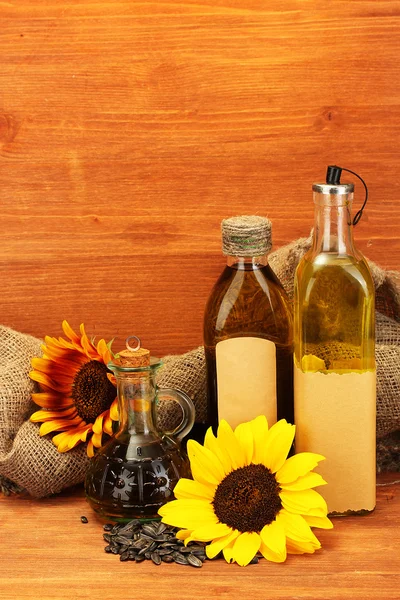 Oil in bottles, sunflowers and seeds, on wooden background — Stock Photo, Image