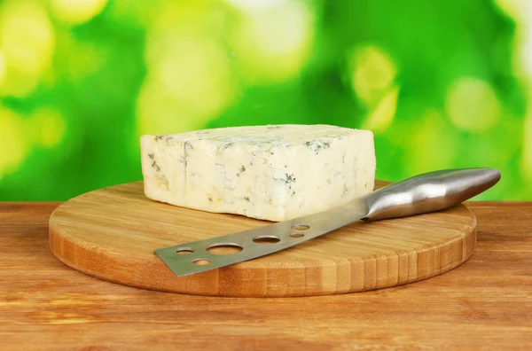 Cheese with mold and knife on the cutting board on bright green background — Stock Photo, Image