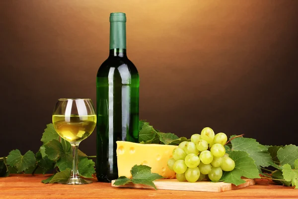 Bottiglia di grande vino con bicchiere e formaggio su tavolo di legno su sfondo marrone — Foto Stock