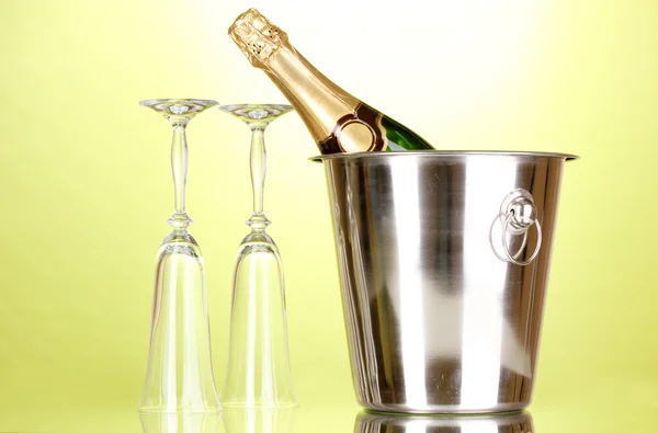 Champagne bottle in bucket with ice and glasses on green background — Stock Photo, Image