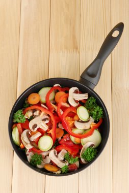 Frying pan with vegetables on wooden background clipart