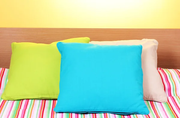 Bright pillows on bed on yellow background — Stock Photo, Image