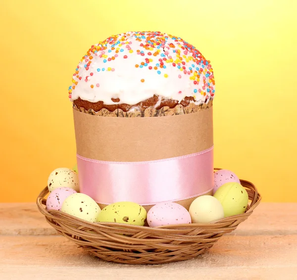 Krásné velikonoční dort v koši s vejce na dřevěný stůl na žlutém podkladu — Stock fotografie