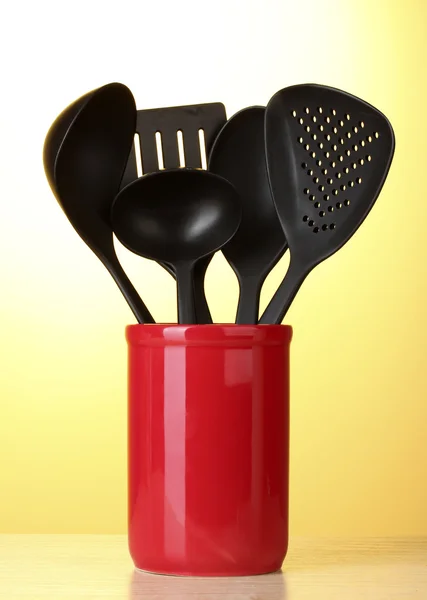Schwarze Küchenutensilien in roter Tasse auf gelbem Hintergrund — Stockfoto
