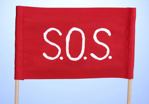 SOS sinal escrito em pano vermelho no fundo azul — Fotografia de Stock