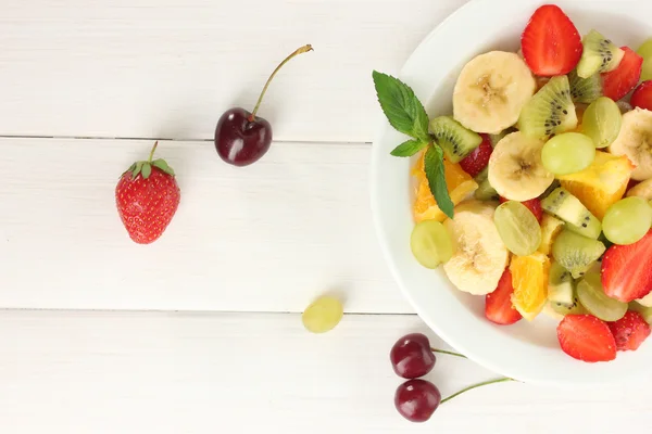 Vers fruit salade op plaat en bessen op witte houten tafel — Stockfoto